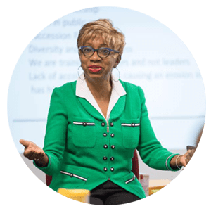 A woman in green jacket and glasses talking.